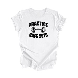 Könnte beinhalten: Weißes T-Shirt mit schwarzem Text "Practice Safe Sets" und einer Grafik einer Langhantel.