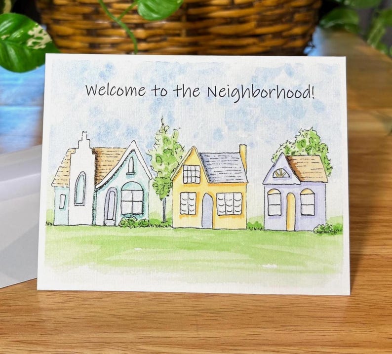 May include: A watercolour greeting card with the text "Welcome to the Neighbourhood!" shows three houses. The houses are white, blue, and yellow, with green grass and trees. The sky is light blue.