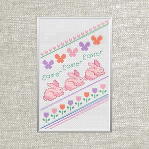 May include: Cross-stitch artwork featuring pink bunnies, tulips, and the word "Easter" in a framed design. The design includes pastel colors like pink, purple, orange, and green, creating a spring or Easter theme.