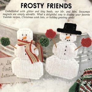 May include: Two white snowman magnets labeled FROSTY FRIENDS. One snowman wears a striped scarf and green mittens, while the other wears a black top hat and red mittens. Both feature orange noses, black bead eyes, and glittery white textures.