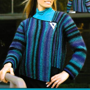 May include: A long-sleeve knit sweater featuring vertical stripes in shades of blue, purple, and black. The sweater has an asymmetrical front closure secured with a white triangular pin. It is worn over a solid turquoise mock neck shirt.