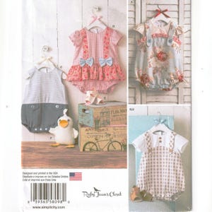 May include: A sewing pattern envelope featuring illustrations of infant rompers and a plush duck. Designs include a pink gingham romper with bows, a floral print romper, a grey and white color-blocked romper, and a tan gingham romper with white sleeves.