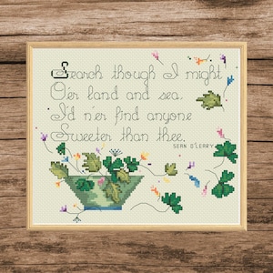 May include: Cross-stitch artwork in a wooden frame. The design features a quote: "Search though I might O'er land and sea. I'd n'er find anyone Sweeter than thee." The artwork includes a green floral arrangement and decorative elements.