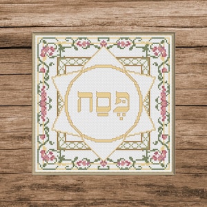Pode incluir: Obra de arte em ponto cruz com um design central da Estrela de David e texto hebraico dourado. O fundo branco é emoldurado por uma borda quadrada com padrões florais e de videira rosa, verde e dourado. A obra de arte está sobre um fundo de madeira.
