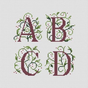 May include: Cross-stitch design featuring the letters A, B, C, and D. Each letter is a deep burgundy color and is adorned with green leaves and small red berries. The background is a plain white fabric.