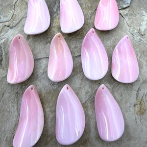 May include: Ten smooth, teardrop-shaped pink shell pendants arranged in three rows. Each piece features a glossy, iridescent finish with subtle white marbling and a small, circular hole drilled near the top for hanging or stringing purposes.