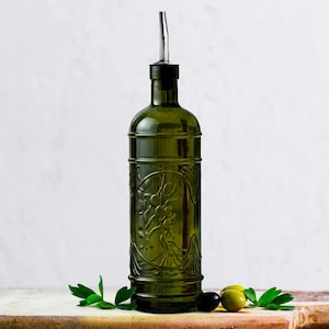 May include: A green glass olive oil bottle with a metal spout and decorative embossed design. The bottle is displayed with olives and greenery on a wooden surface, suggesting a kitchen or dining theme.