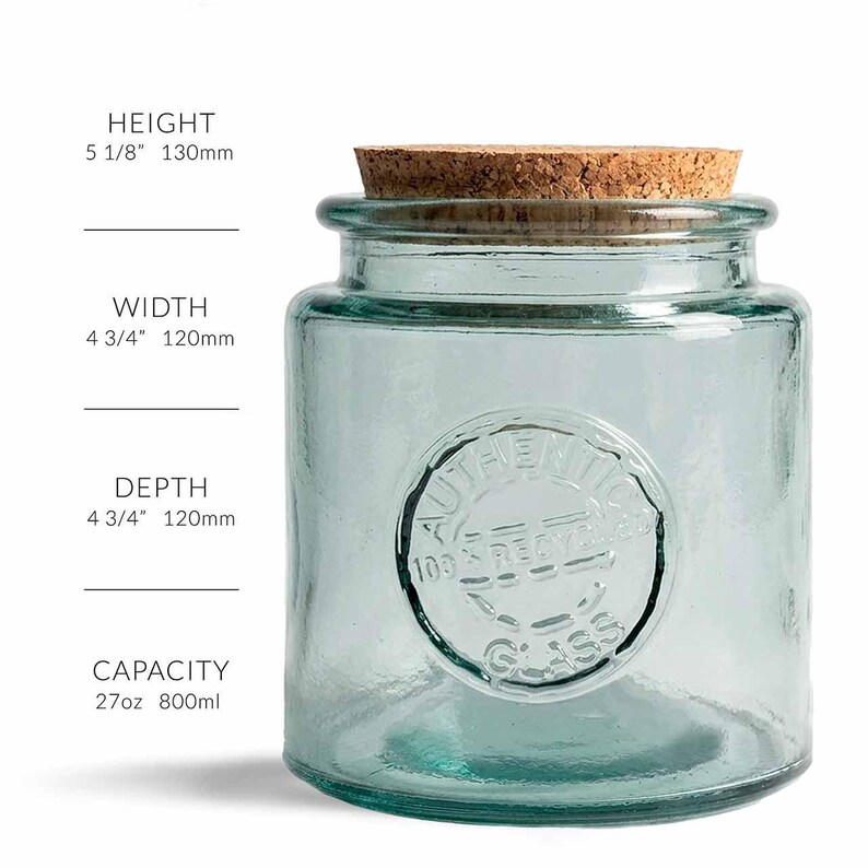 May include: A clear, turquoise-colored glass jar with a cork lid. The jar is cylindrical with a rounded base and a circular embossed design that reads "AUTHENTIC 100% RECYCLED GLASS". The jar is 5 1/8" high, 4 3/4" wide, and 4 3/4" deep, with a capacity of 27oz.