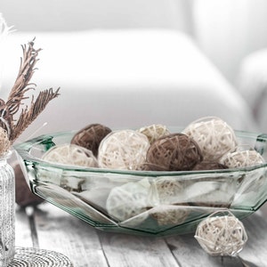 May include: A clear glass bowl with a faceted design, filled with brown and white decorative balls. The bowl is sitting on a white wooden surface.