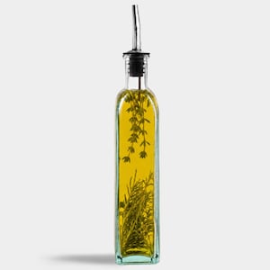 May include: A tall, square, clear glass bottle filled with golden yellow oil, containing sprigs of green rosemary and thyme. The bottle is topped with a silver-colored metal pourer spout featuring a black rubber seal at the neck of the glass container.