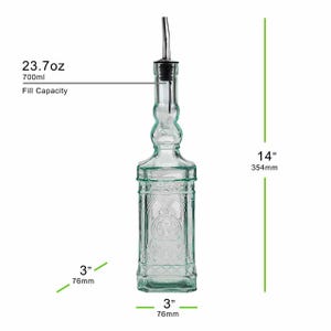 Op de afbeelding: Een heldere glazen fles met een roestvrijstalen tuit, ontworpen voor het doseren van vloeistoffen. De fles is 354 mm hoog, 76 mm breed en heeft een vulcapaciteit van 700 ml. Het heeft een reli&euml;f ontwerp en een zwarte stopper.