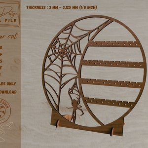 May include: A wooden earring holder shaped like a spider web with a spider in the center. The holder has three shelves for earrings and a stand to keep it upright. The text "THICKNESS: 3 MM - 3,125 MM (1/8 INCH)" is visible at the top of the image.