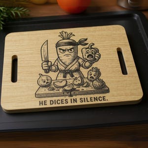 May include: A light-colored wooden cutting board with a humorous illustration of a carrot ninja holding a knife and a pepper. The text "HE DICES IN SILENCE" is below the illustration. Two handle cutouts are on the sides.