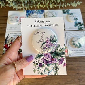 May include: Thank you for celebrating with us, Marry & John. A white card with purple and green floral design and a round button with the same design and the text "Marry & John".