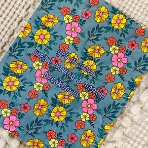 May include: A teal floral print with yellow, pink, and orange flowers and green leaves. The text "get in loser, we're having a mental breakdown" is in a purple font.