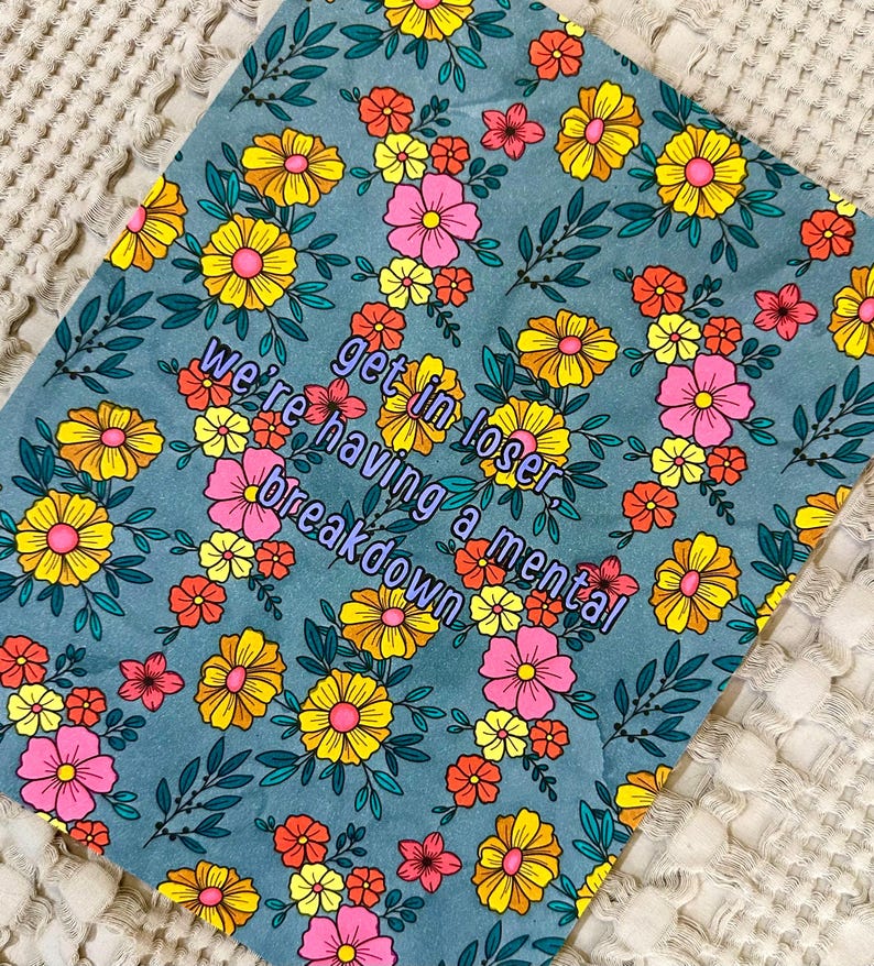 May include: A teal floral print with yellow, pink, and orange flowers and green leaves. The text "get in loser, we're having a mental breakdown" is in a purple font.