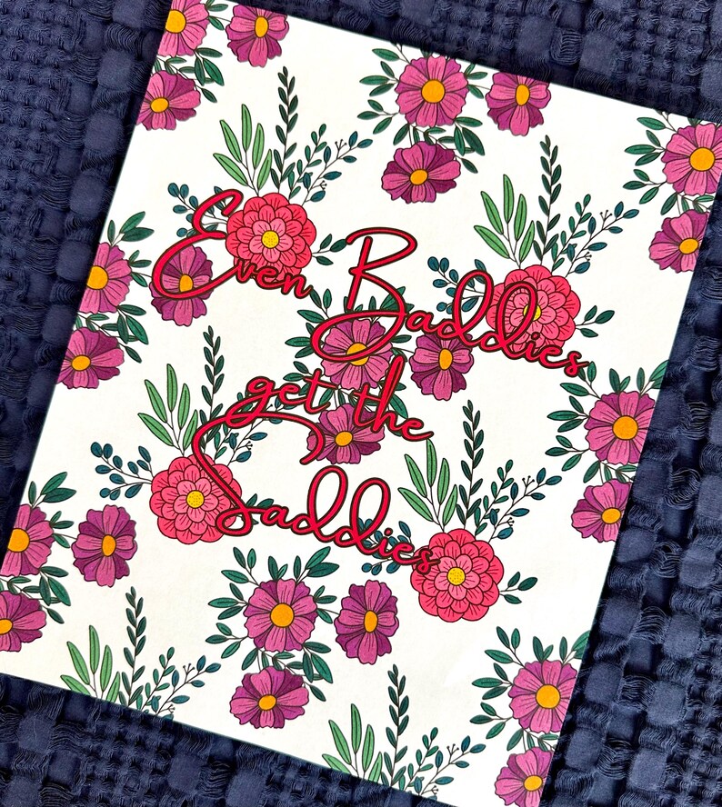 May include: A white canvas print featuring a floral design with pink and purple flowers and green leaves. The text "Even Baddies get the Baddies" is written in a cursive red font.