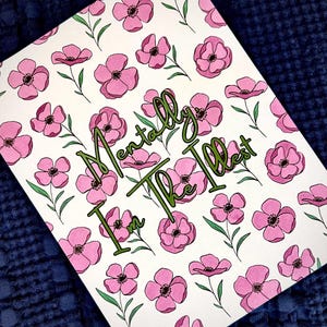 May include: A white card featuring a pattern of pink flowers with green stems and leaves. The words "I'm Mentally The Illest" are written in green cursive script across the center of the card.