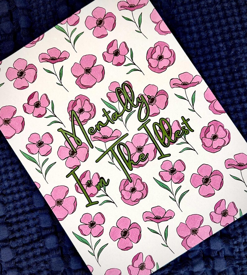 May include: A white card featuring a pattern of pink flowers with green stems and leaves. The words "I'm Mentally The Illest" are written in green cursive script across the center of the card.