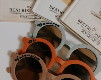 May include: Three pairs of round, colourful sunglasses with UV400 protection. The sunglasses are labelled with the names "Cameron", "Oli", and "Valentina".