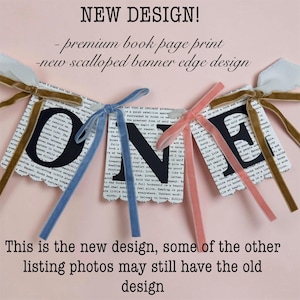 May include: A decorative banner spelling the word ONE with black letters on white book page print paper. The banner features a scalloped edge design and is accented with velvet ribbons in shades of gold, blue, and pink tied at the top corners.