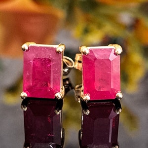 Puede incluir: Un par de pendientes de oro con piedras preciosas rojas de corte esmeralda. Los pendientes tienen un diseño sencillo y son perfectos para el uso diario.