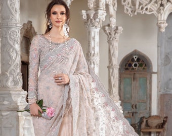 May include: A woman wearing a light pink and silver embroidered saree with a delicate floral pattern. The saree has a sheer, net-like fabric and is adorned with intricate beading and sequins. The woman is holding a single pink rose.