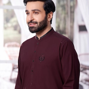 Può includere: Una camicia a maniche lunghe color borgogna con colletto alla coreana e un piccolo disegno ricamato sul petto.