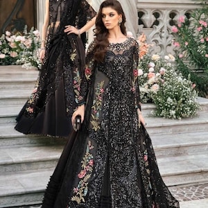 Op de afbeelding: Een zwarte jurk met ingewikkelde borduursels en pailletten. De jurk heeft een lange sleep en een aansluitend lijfje. De stof is doorschijnend en delicaat.