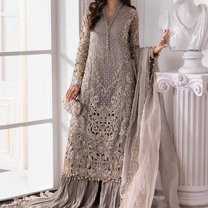May include: A long, gray embroidered formal dress with intricate floral patterns and bead embellishments. The dress features long sleeves, a flowing skirt, and a matching sheer scarf. A small, embellished clutch is held at the waist.
