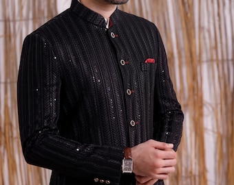 May include: A black formal jacket with a textured pattern and a mandarin collar. The jacket features red accents, a small pocket square, and gold buttons. A brown leather watch with a rectangular face is visible.
