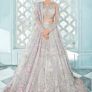 May include: A silver and pink bridal lehenga with intricate embroidery and embellishments. The lehenga has a long, flowing skirt and a fitted bodice. The dupatta is a sheer fabric with a delicate floral pattern.