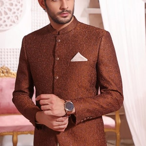 May include: A brown patterned blazer with a mandarin collar and a single button fastening. The blazer has a pocket on the left side with a white handkerchief. The blazer is worn over a white shirt and trousers.