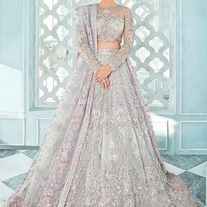 May include: A silver and pink bridal lehenga with intricate embroidery and embellishments. The lehenga has a long, flowing skirt and a fitted bodice. The dupatta is a sheer fabric with a delicate floral pattern.