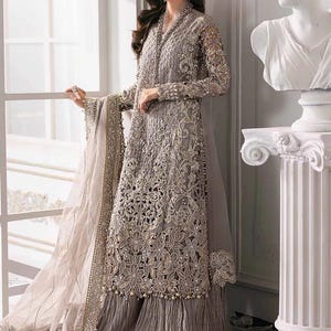 May include: A long, intricately embroidered gray dress with a matching sheer shawl. The dress features detailed floral patterns, bead embellishments, and a pleated skirt. The sleeves are long and sheer, and the dress has a high neckline.