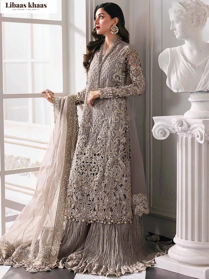 May include: A long, intricately embroidered gray dress with a matching sheer shawl. The dress features detailed floral patterns, bead embellishments, and a pleated skirt. The sleeves are long and sheer, and the dress has a high neckline.