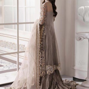 May include: A long, flowing, gray dress with intricate embroidery and embellishments. The dress features sheer sleeves and a matching shawl with detailed trim. The design includes floral patterns and beadwork, creating an elegant and sophisticated look. The dress is suitable for formal events.