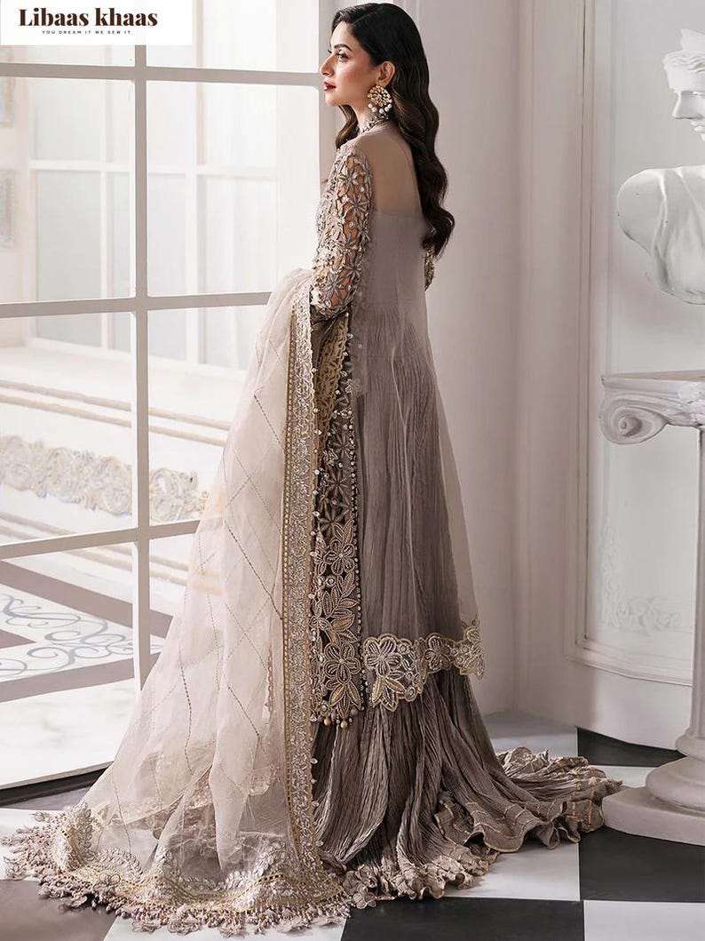 May include: A long, flowing, gray dress with intricate embroidery and embellishments. The dress features sheer sleeves and a matching shawl with detailed trim. The design includes floral patterns and beadwork, creating an elegant and sophisticated look. The dress is suitable for formal events.