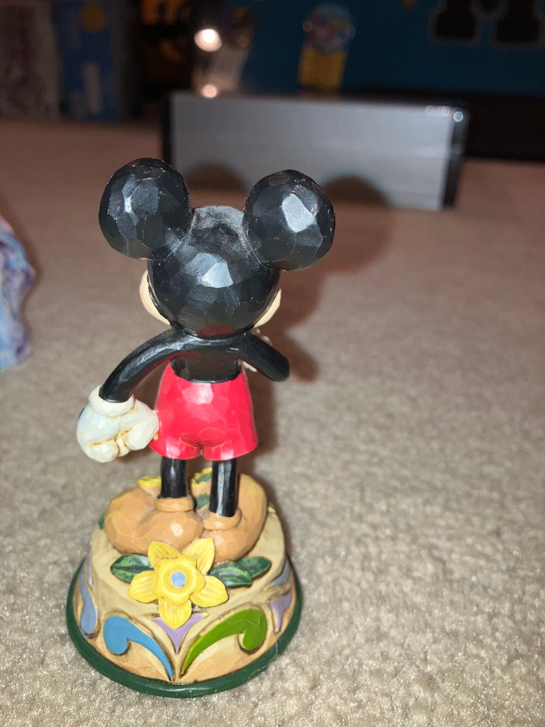 Pu&ograve; includere: Una statuetta in ceramica dipinta a mano di Topolino con pantaloncini rossi e scarpe nere. &Egrave; in piedi su una base colorata con un fiore giallo.