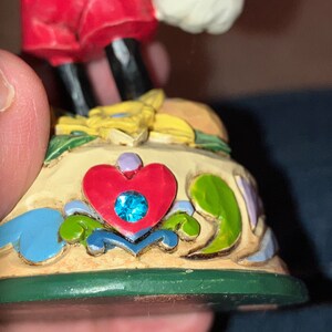 Pu&ograve; includere: Una statuetta in ceramica dipinta a mano di Topolino in piedi su una base con un design a forma di cuore e un gioiello blu. La base &egrave; decorata con fiori e foglie.