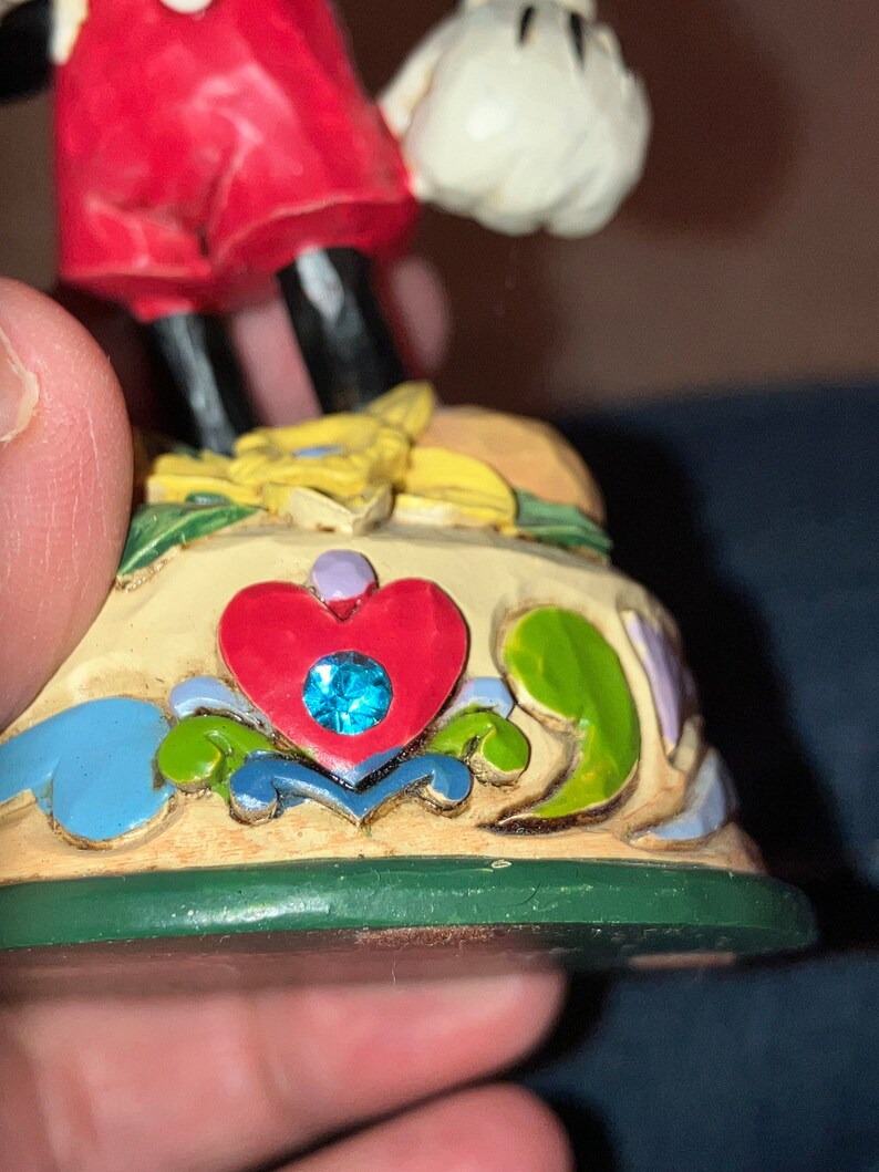 Pu&ograve; includere: Una statuetta in ceramica dipinta a mano di Topolino in piedi su una base con un design a forma di cuore e un gioiello blu. La base &egrave; decorata con fiori e foglie.