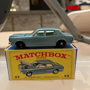 May include: A blue Matchbox Series 53 die-cast car model in its original box. The box is yellow with red lettering and features a picture of the car with its hood open.
