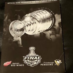 May include: A black and white program cover for the 2009 Stanley Cup Final. The cover features a silver Stanley Cup trophy, the words "Stanley Cup Final 2009", and the logos for the Detroit Red Wings and the Pittsburgh Penguins.