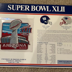 May include: A commemorative patch for Super Bowl XLII, featuring the Lombardi Trophy, the words "Super Bowl XLII" and "Arizona" with the date "02.03.08". The patch is surrounded by a red, white, and blue border. The text "New York Giants 17" and "New England Patriots 14" is displayed above the starting lineups for both teams. The text "Most Valuable Player Eli Manning" is displayed at the bottom of the image.