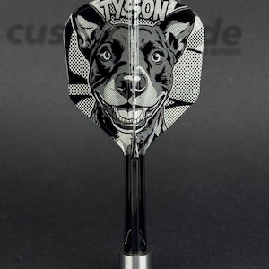 May include: A black and white dart featuring a smiling dog illustration. The word "TYSON" is printed above the dog's head. The dart has a black shaft and a silver base.