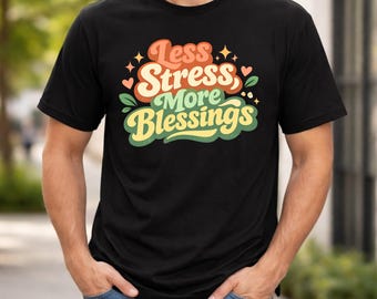 May include: Black t-shirt with the text "Less Stress, More Blessings" in a retro font. The design includes orange, green, and red accents with stars and hearts. The shirt is short-sleeved.