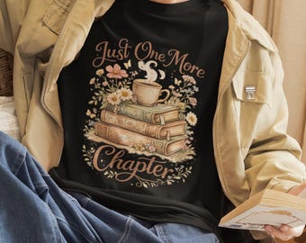 May include: A black t-shirt featuring a graphic print of a stack of three vintage-style books topped with a steaming cup of coffee, surrounded by colorful flowers and butterflies, with the text "Just One More Chapter" in a decorative script font.
