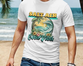 May include: A white short-sleeve t-shirt featuring a circular graphic of a beach scene with a palm tree, ocean waves, and flowers. The text SALT AIR is printed in yellow above the circle, and the text Good Vibes is in teal script below.