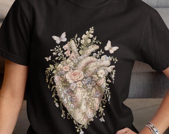 May include: A black short-sleeved t-shirt featuring a central graphic of an anatomical heart intertwined with various pastel-colored flowers, including roses and small blossoms, accented by several delicate butterflies surrounding the floral arrangement.