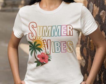 May include: A cream-colored short-sleeve t-shirt featuring the text "SUMMER VIBES" in colorful outlined letters. The graphic includes a yellow sun, a green palm tree, and a vibrant red hibiscus flower positioned below the text on the front.